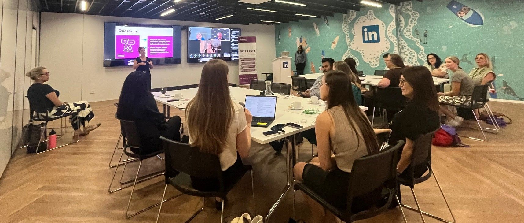 Photo of attendees at the LinkedIn office, sat at tables as content delivered in front of a screen with online guests